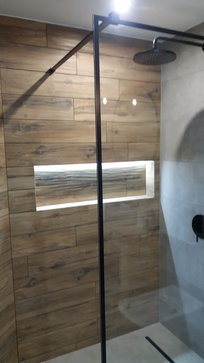 Łazienka walk-in z drewnopodobnymi płytkami, podświetlaną wnęką i czarną deszczownicą