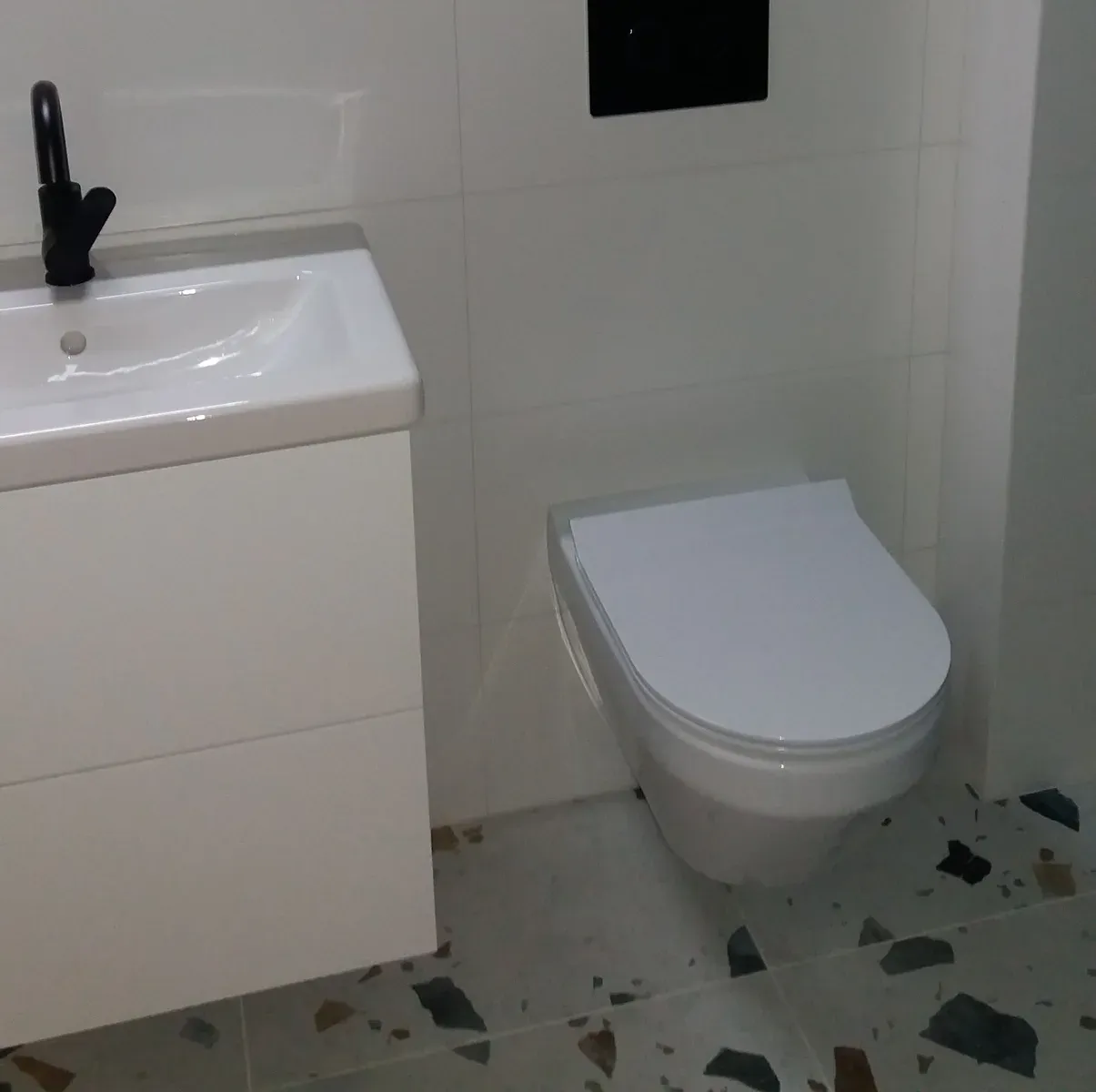 Umywalka z czarną baterią i podwieszany WC nad podłogą lastryko (terrazzo)