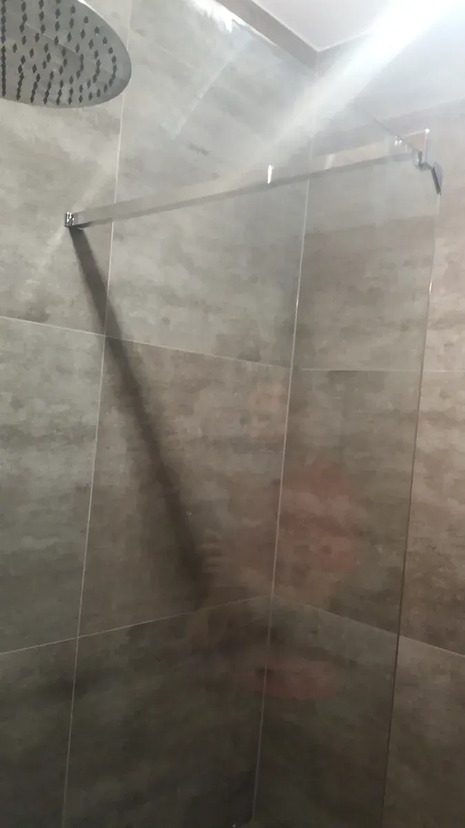 Szklana ścianka walk-in w chromowanym profilu na tle grafitowego betonu