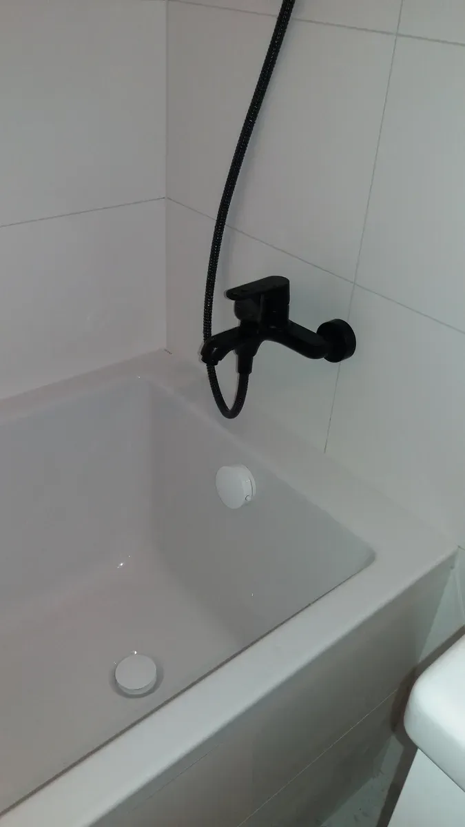 Wanna akrylowa z czarną baterią ścienną na tle białych płytek