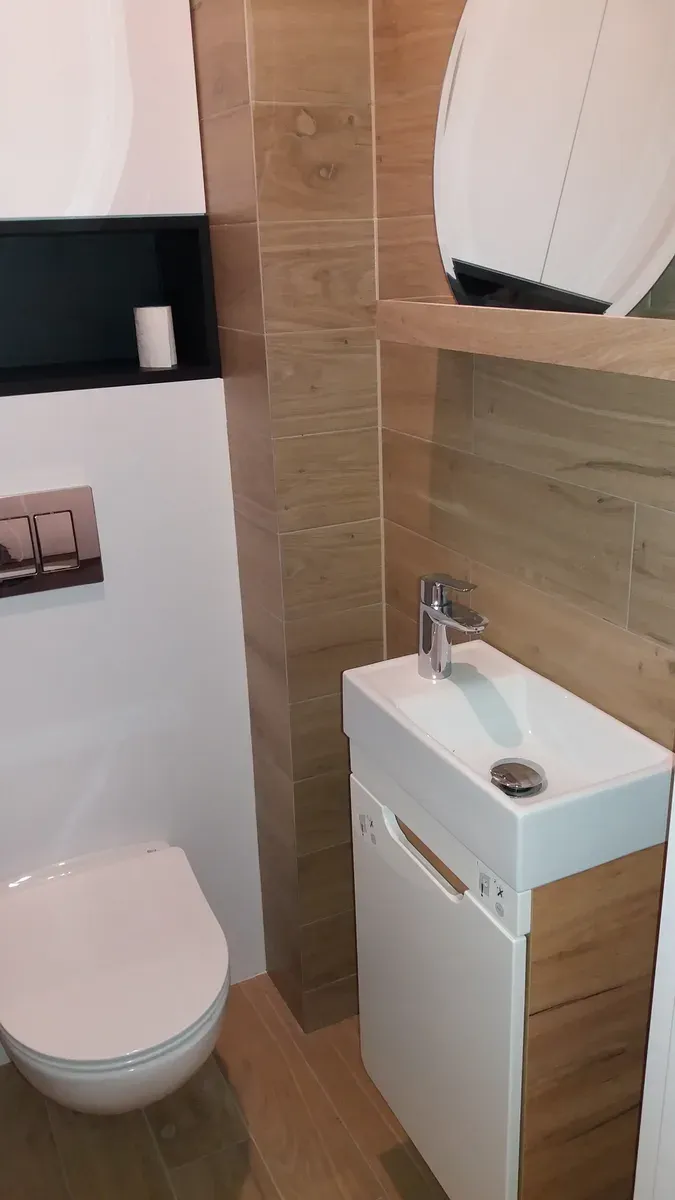 Strefa umywalki i WC podwieszanego na tle płytek drewnopodobnych — łazienka na poddaszu